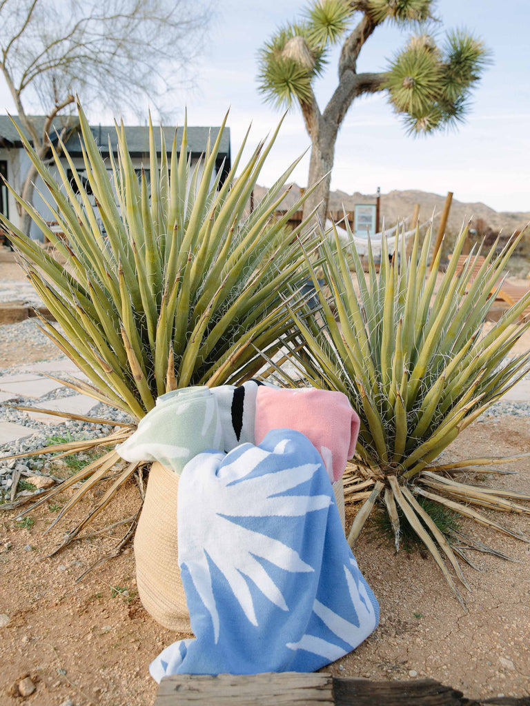 Blue and white, green and white, and pink and white tropical patterned cabana beach towels folded in a basket in the desert.