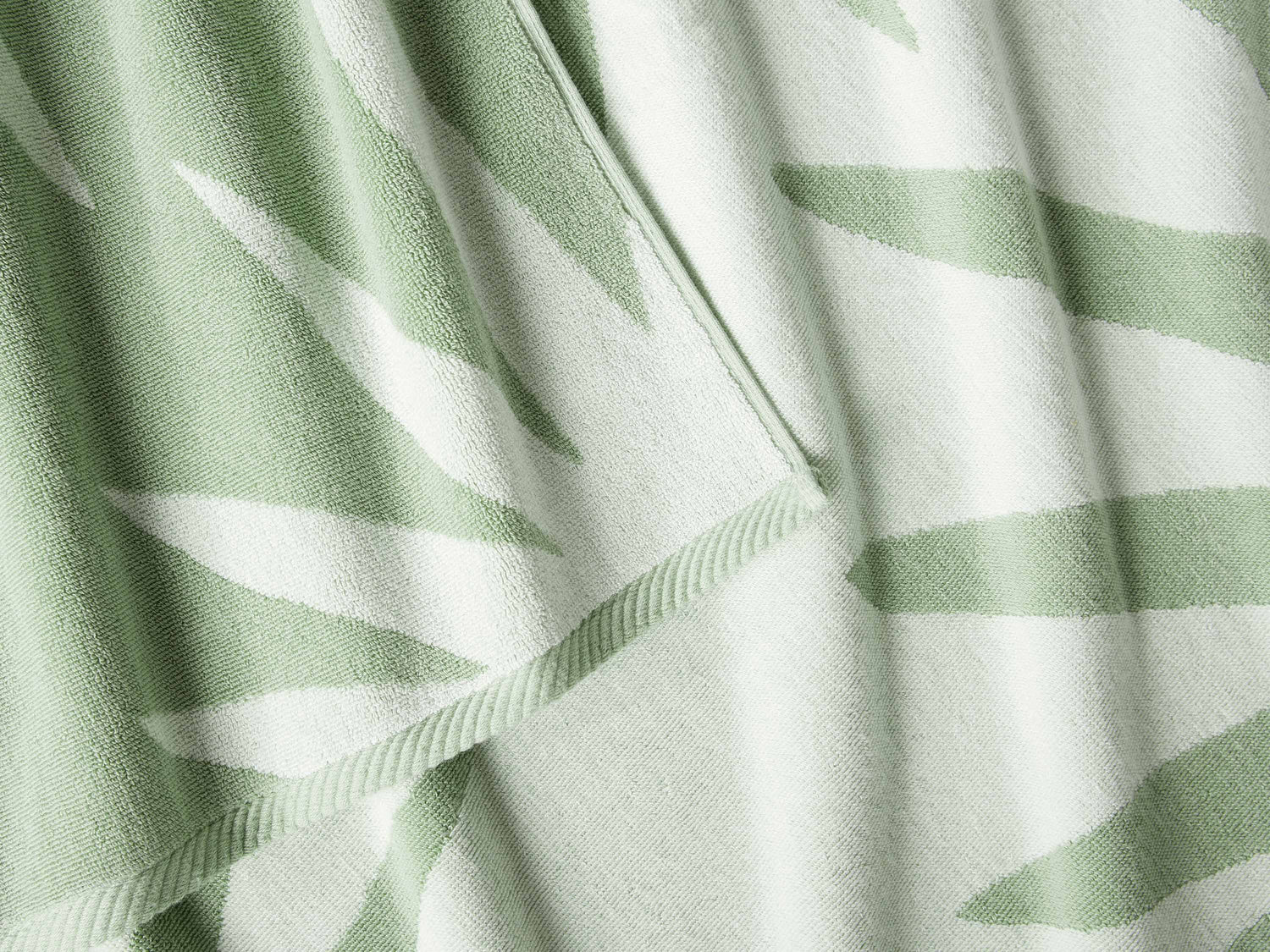 A close-up of a thick and soft, green and white tropical patterned cabana beach towel.