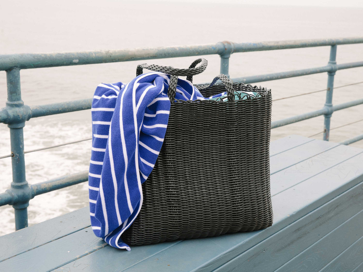 Oversized black beach bag with striped towel on a pier.