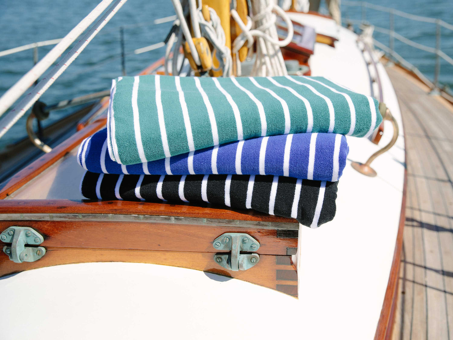 A stack of folded, green and white, blue and white, and black and white striped cabana beach towels on a sailboat.