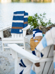 A pair of chairs next to the water with Mexican Blankets draped over them.