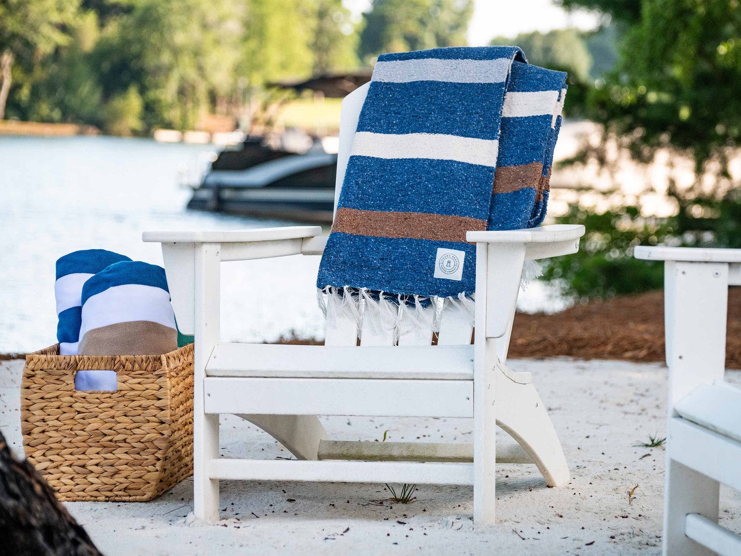 A blue, white, and brown striped Mexican Blanket draped over a white chair on the sand.