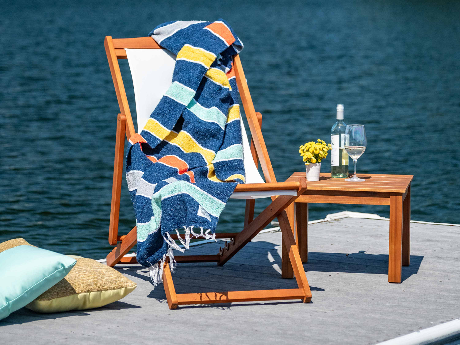 A blue, yellow, orange, and teal striped Mexican Blanket draped over a chair by the water.
