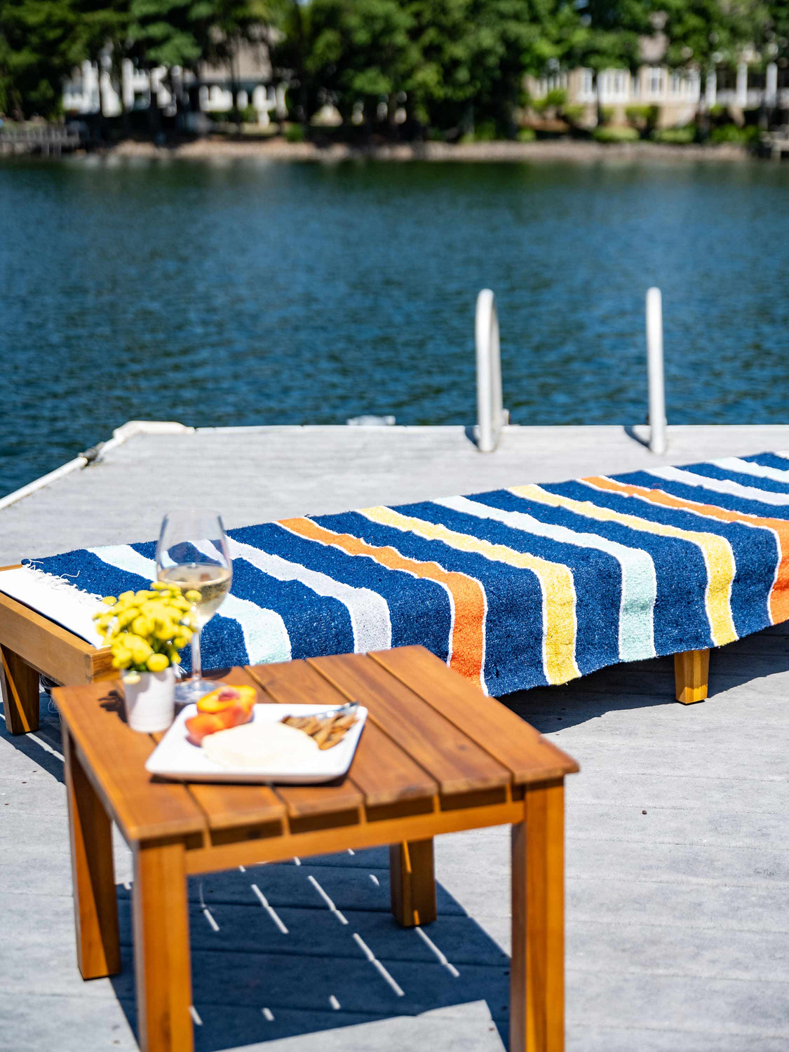 A lounge chair next to the water with a multicolored striped Mexican Blanket laid out on top of it.