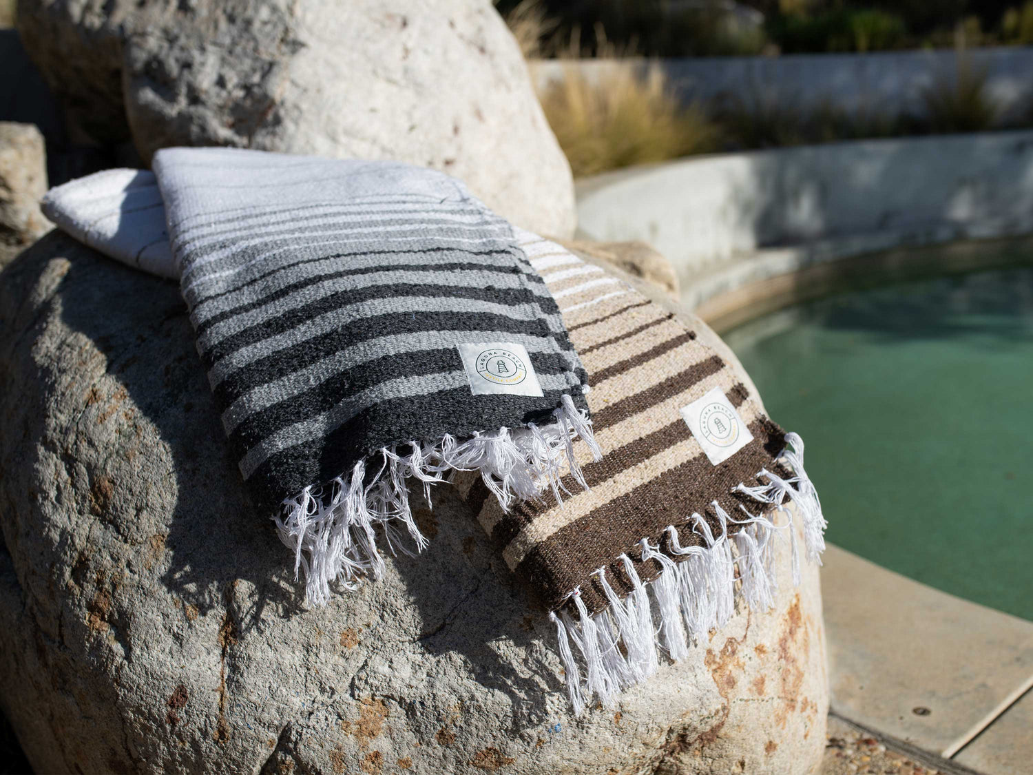White and grey soft and luxurious Mexican blankets outdoors, next to a pool.