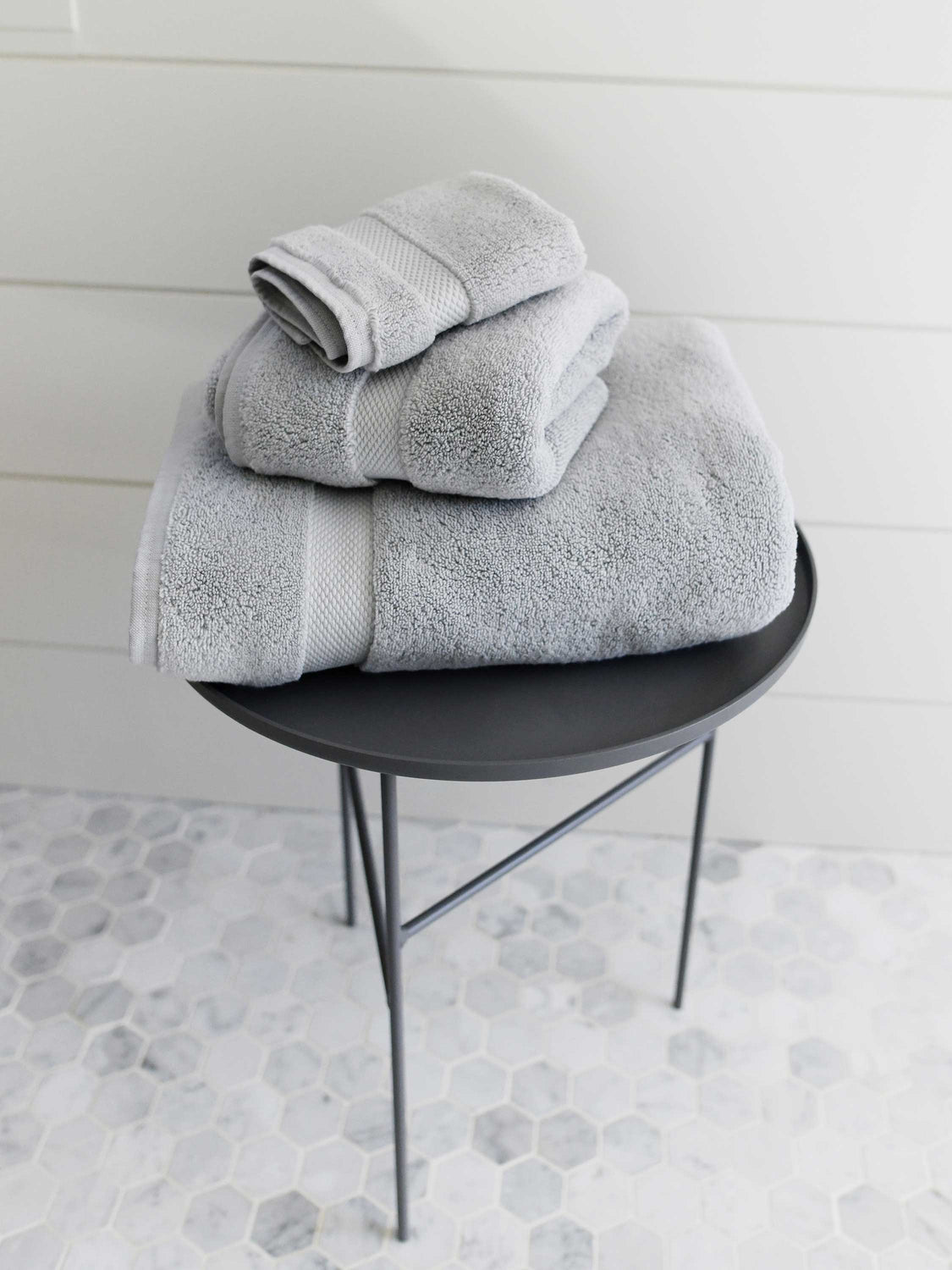 A set of gray cotton bath towels folded and stacked on one another on top of a side table.