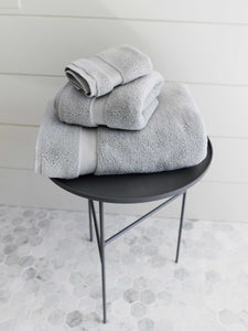 A set of gray cotton bath towels folded and stacked on one another on top of a side table.