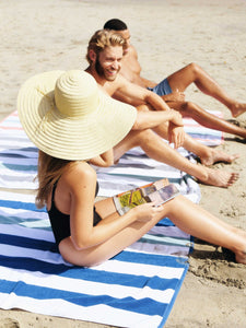 A woman and two men sitting on striped cabana beach towels having a good time at the beach.