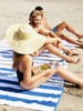 A woman and two men sitting on striped cabana beach towels having a good time at the beach.
