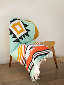 A green, red, and yellow patterned Mexican throw blanket draped over an indoor chair.