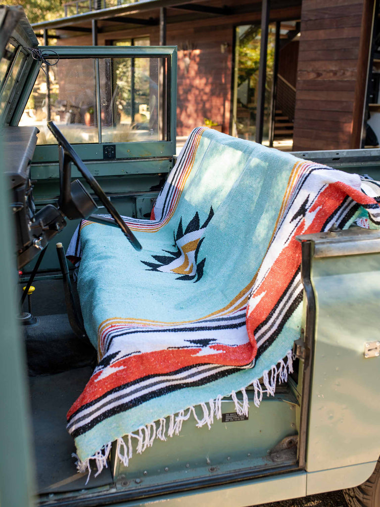 A green, red, and yellow patterned Mexican blanket covering the front seat of a car.