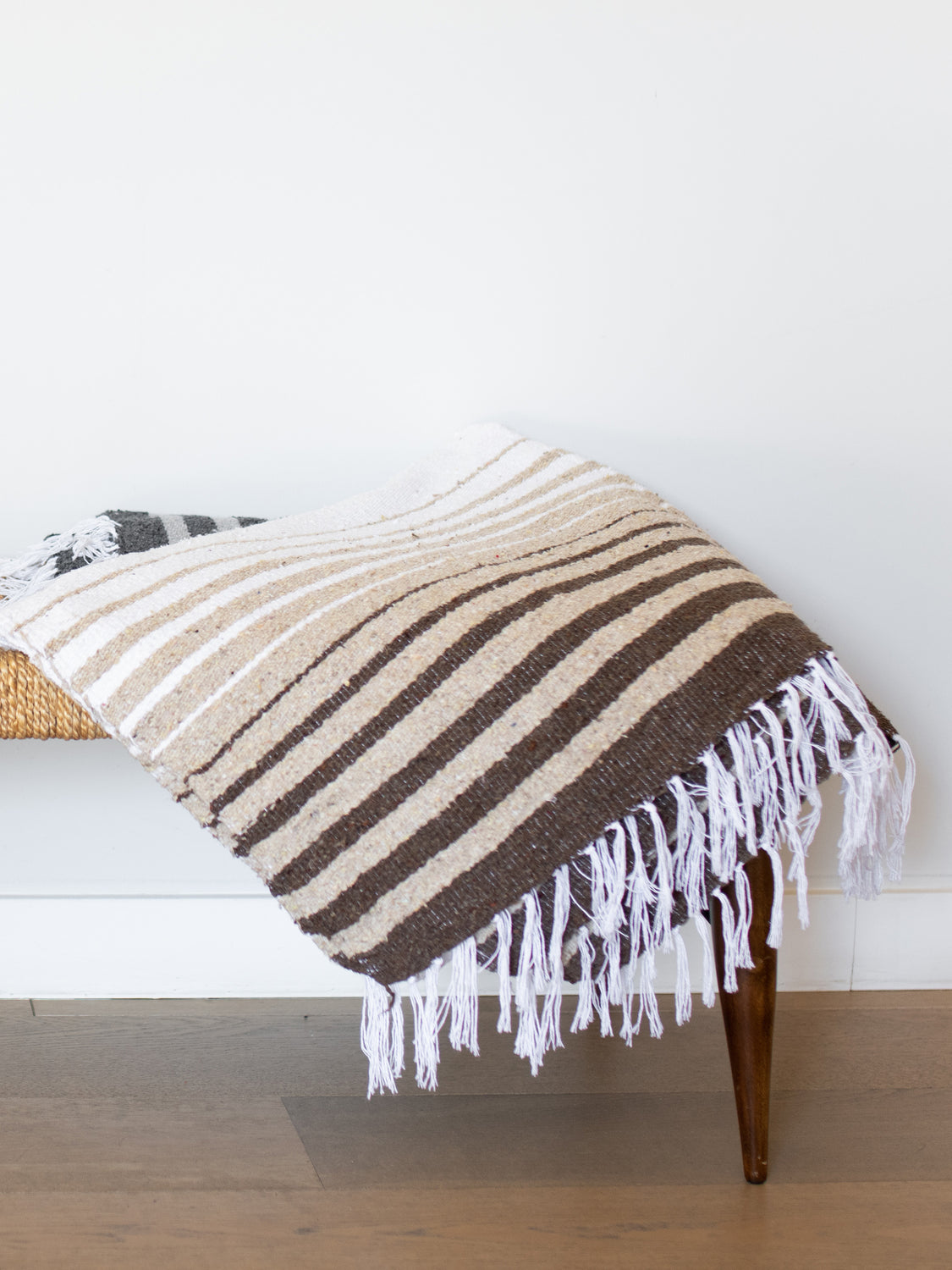 A hand-woven, brown striped Mexican blanket folded on top of a wicker bench.