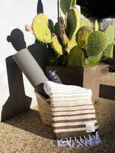 Oversized, brown striped Mexican blanket draped over a woven basket with a gray yoga mat and water bottle inside.