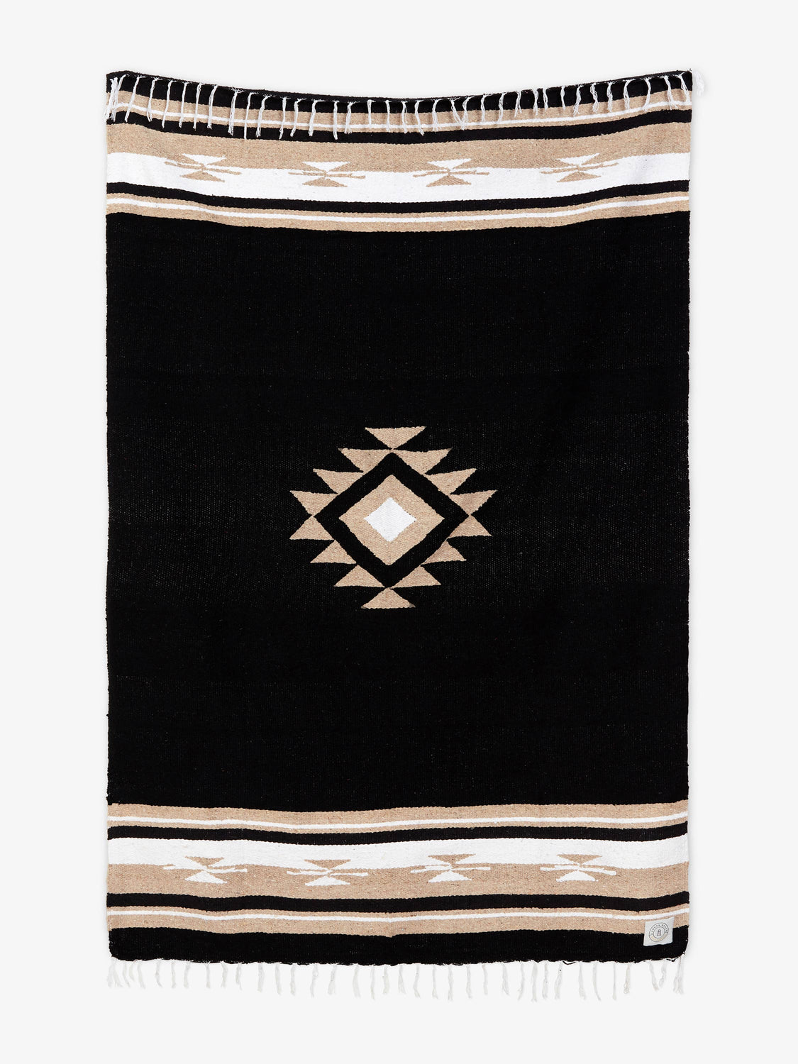 Oversized, traditional Mexican blanket in black, tan, and white pattern with white fringe spread out.