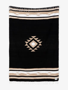 Oversized, traditional Mexican blanket in black, tan, and white pattern with white fringe spread out.