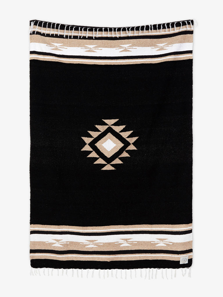 Oversized, traditional Mexican blanket in black, tan, and white pattern with white fringe spread out.