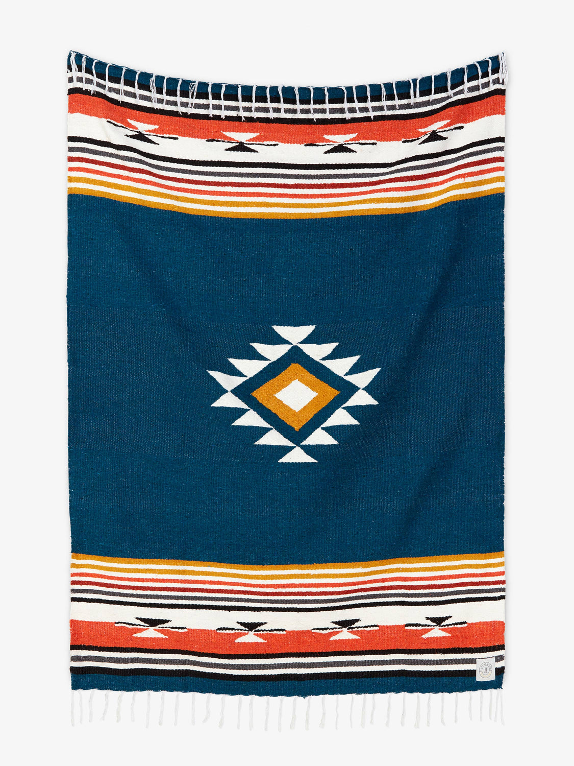 Oversized, traditional Mexican blanket in navy blue, red, and yellow pattern with white fringe spread out.