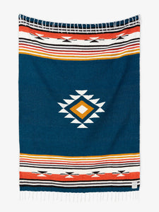 Oversized, traditional Mexican blanket in navy blue, red, and yellow pattern with white fringe spread out.