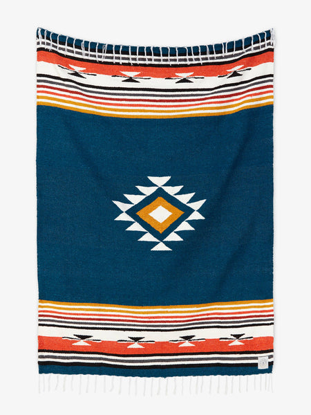 Oversized, traditional Mexican blanket in navy blue, red, and yellow pattern with white fringe spread out.