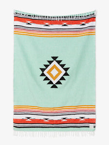 Oversized, traditional Mexican blanket in green, red, and yellow pattern with white fringe spread out.