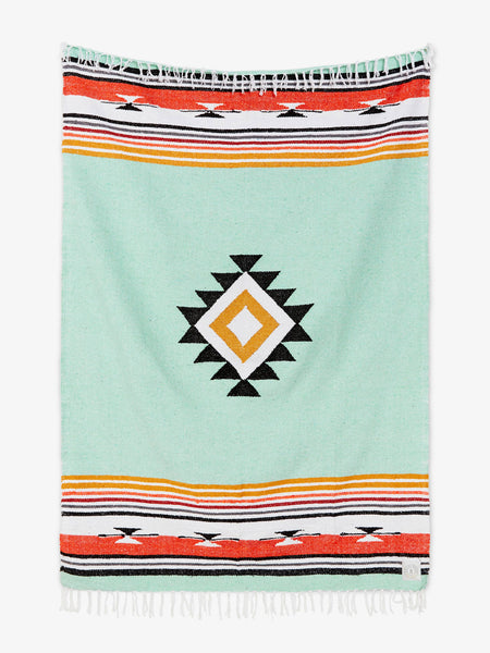 Oversized, traditional Mexican blanket in green, red, and yellow pattern with white fringe spread out.