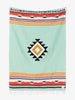 Oversized, traditional Mexican blanket in green, red, and yellow pattern with white fringe spread out. 
