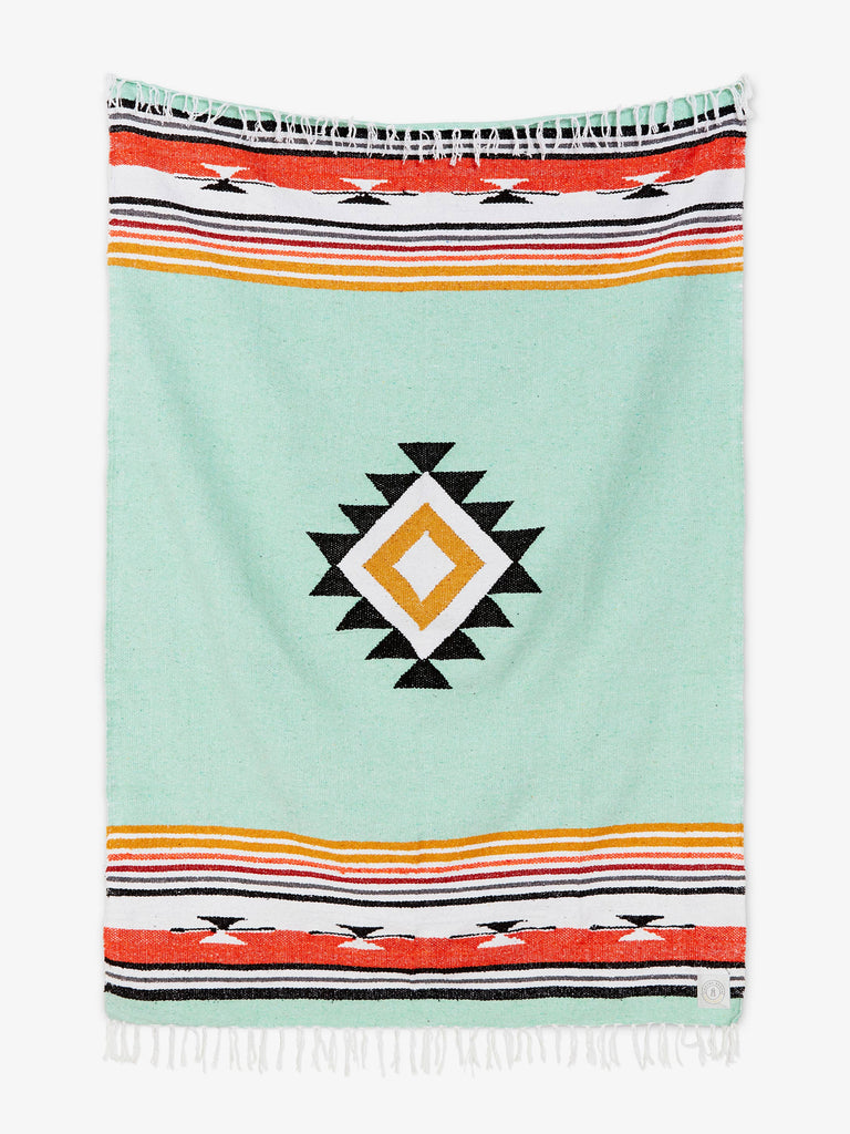 Oversized, traditional Mexican blanket in green, red, and yellow pattern with white fringe spread out.