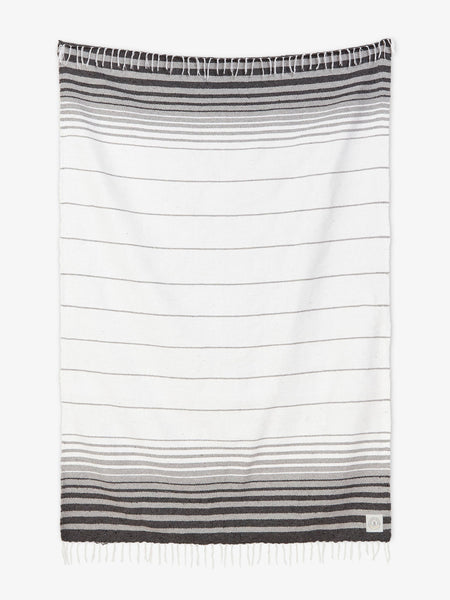 Oversized, traditional Mexican blanket in gray and white stripe design with white fringe spread out.