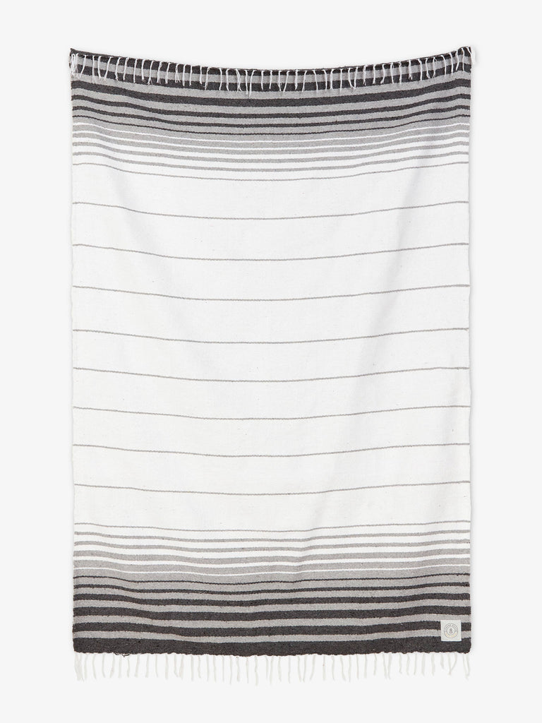 Oversized, traditional Mexican blanket in gray and white stripe design with white fringe spread out.