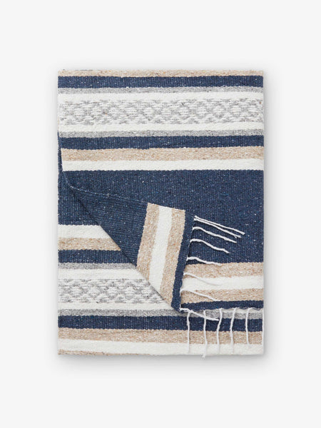 A folded traditional, hand-woven Mexican blanket in gray, tan, and white pattern with fringe.