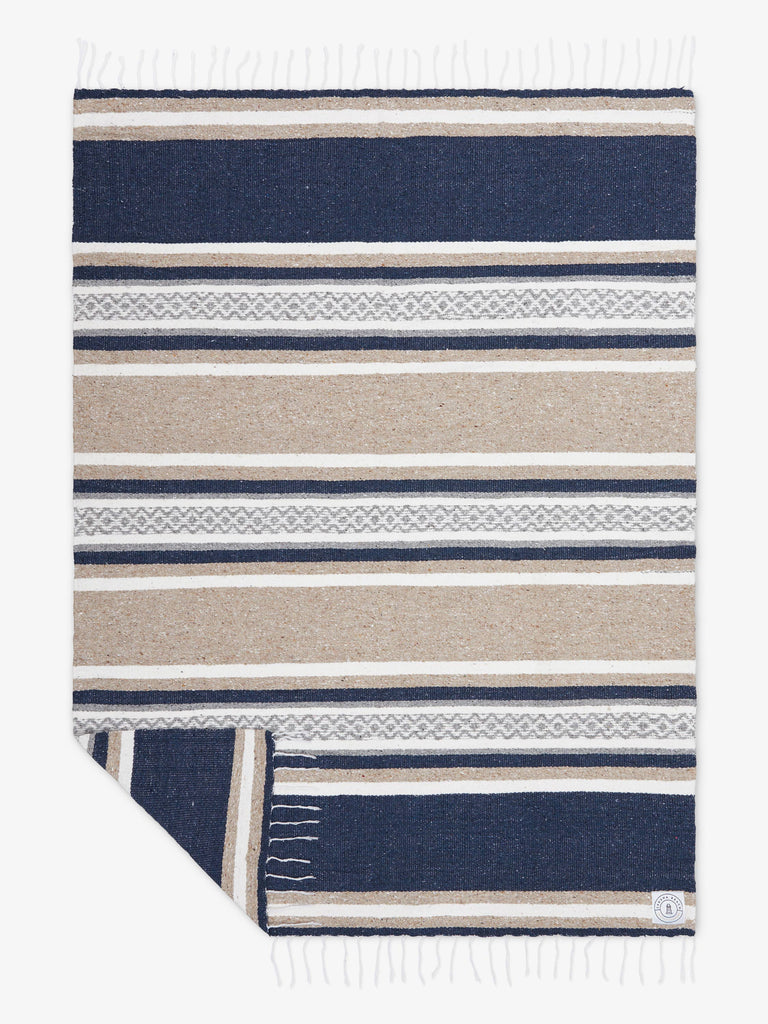 Oversized, traditional Mexican blanket in gray, tan, and white pattern with white fringe spread out.