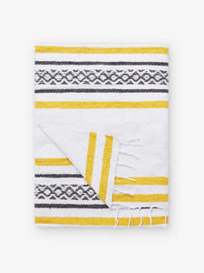 A folded traditional, hand-woven Mexican blanket in yellow and white pattern with fringe.