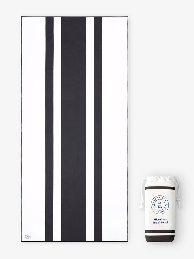 An oversized, quick drying black and white striped microfiber beach towel laid out next to a matching travel bag.