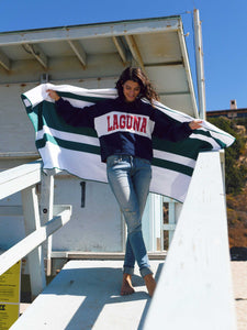 A woman standing on a lifeguard tower ramp holding an extra large green striped microfiber beach towel spread out behind her.