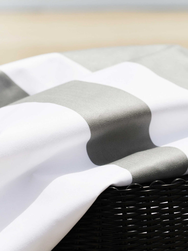 A close-up of an oversized, quick drying gray and white striped microfiber beach towel laid atop a beach bag in the sand.