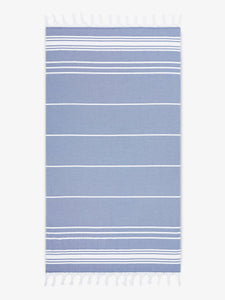 An oversized, blue and white striped Turkish cotton towel with white fringe laid out.