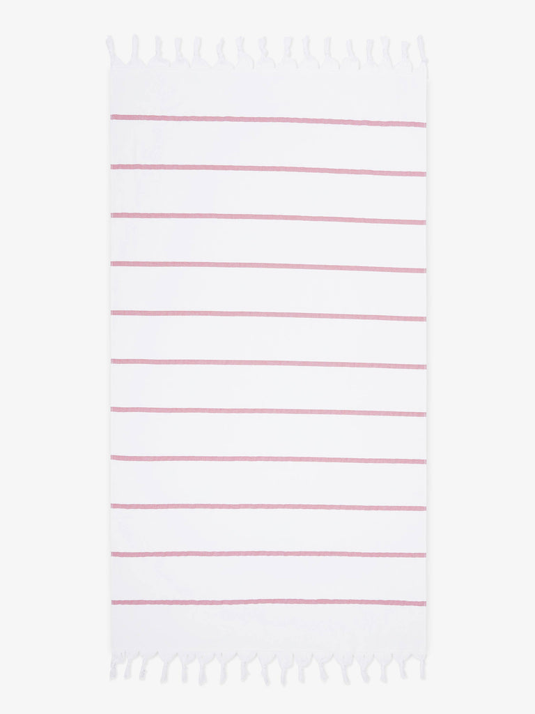 An oversized, white and pink striped Turkish cotton towel with white fringe laid out.