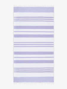 An oversized, white and purple striped Turkish cotton towel with white fringe laid out.