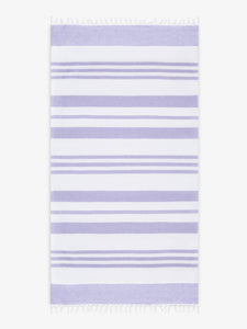 An oversized, white and purple striped Turkish cotton towel with white fringe laid out.