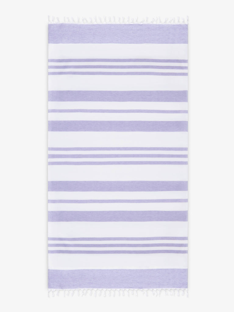 An oversized, white and purple striped Turkish cotton towel with white fringe laid out.