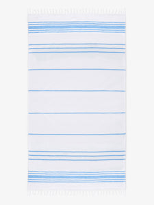 An oversized, white and light blue striped Turkish cotton towel with white fringe laid out.