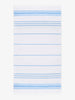 An oversized, white and light blue striped Turkish cotton towel with white fringe laid out.