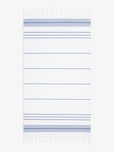 An oversized, white and blue striped Turkish cotton towel with white fringe laid out.