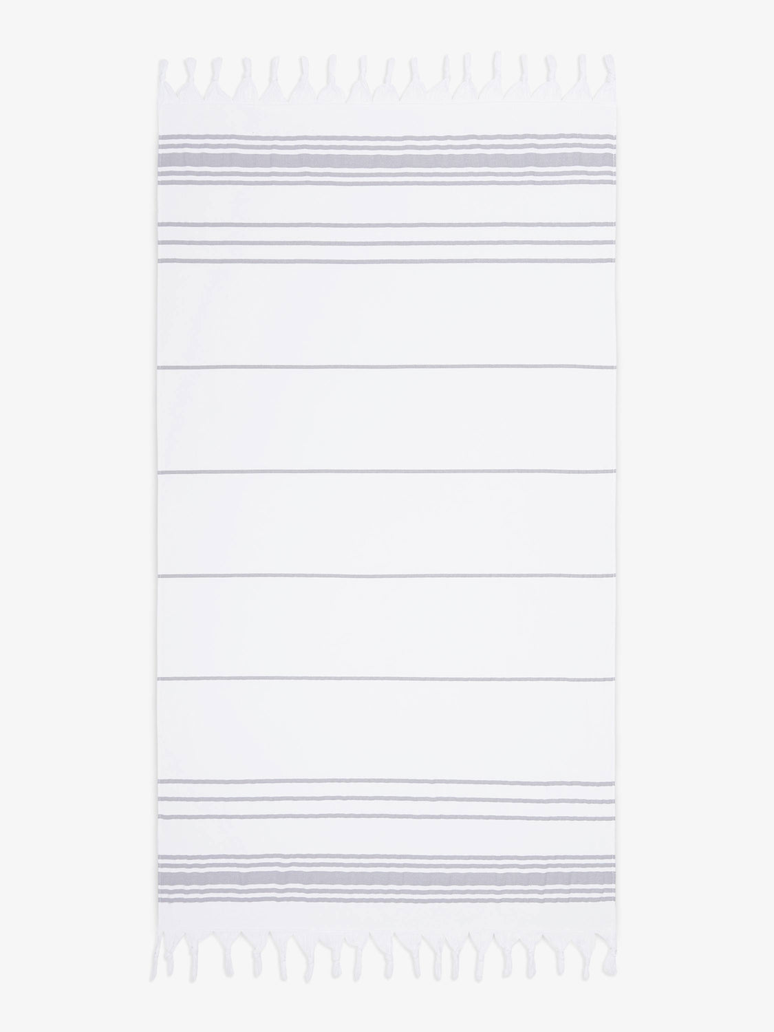An oversized, white and gray striped Turkish cotton towel with white fringe laid out.