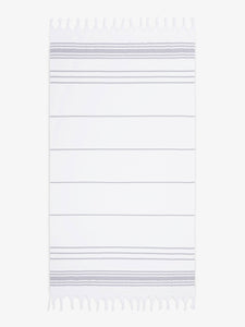 An oversized, white and gray striped Turkish cotton towel with white fringe laid out.