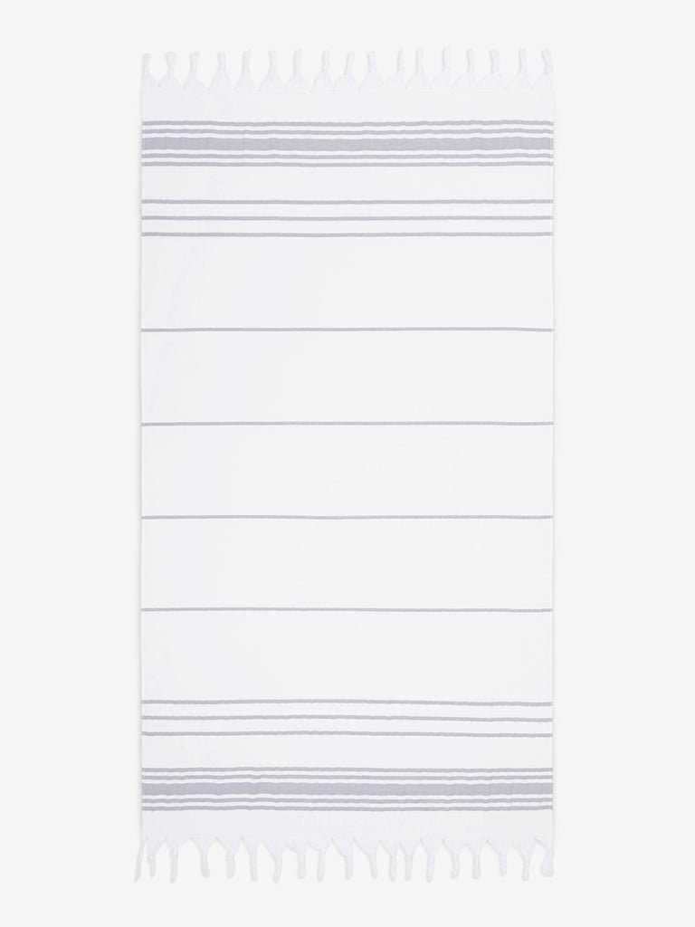 An oversized, white and gray striped Turkish cotton towel with white fringe laid out.