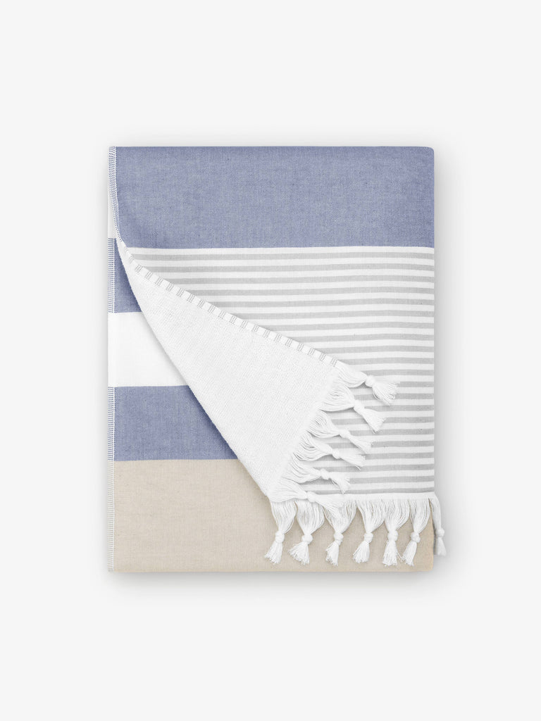 A folded blue, white, and tan striped Turkish hand towel with white fringe.