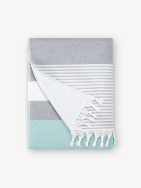 A folded teal and gray striped Turkish towel with white fringe.