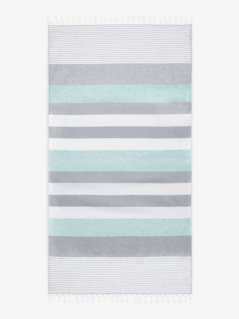 An oversized, teal and gray striped Turkish cotton towel with white fringe laid out.