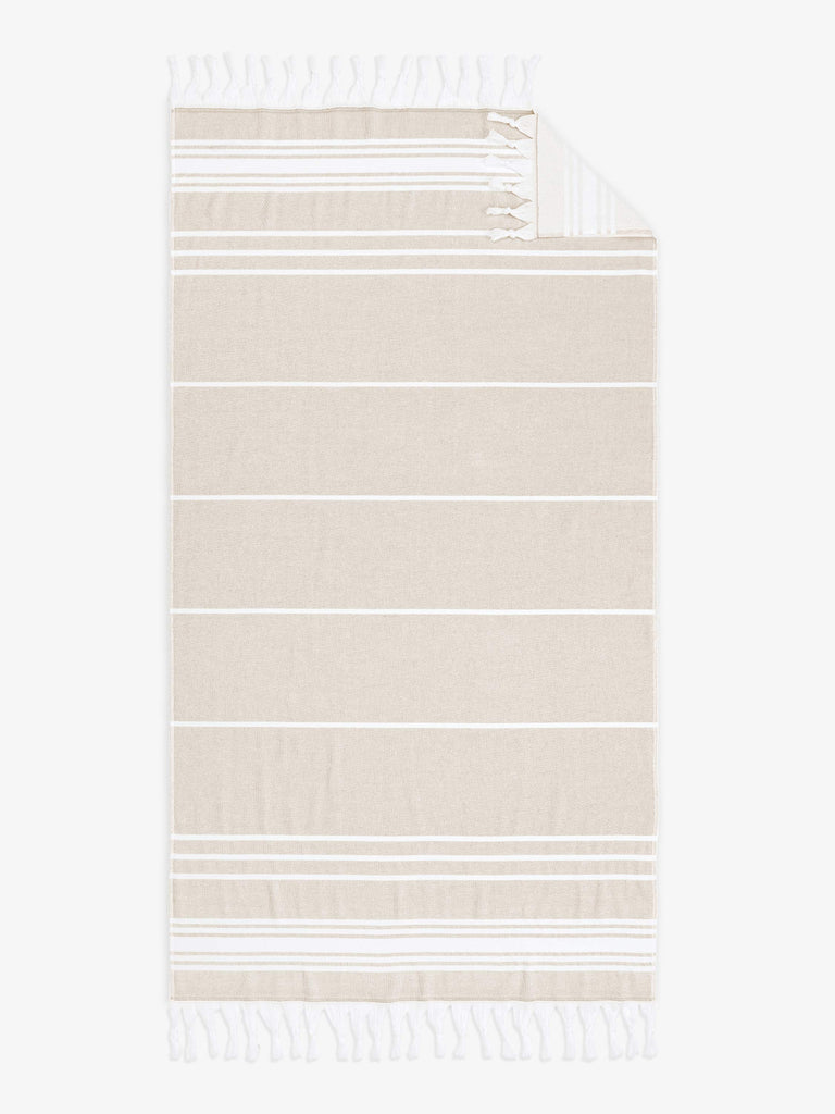 An oversized, tan and white striped Turkish cotton towel with white fringe laid out.